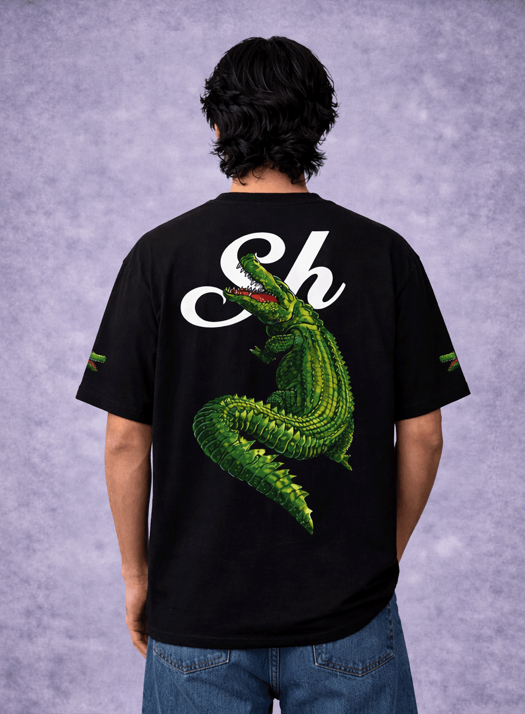 Person wearing a black t-shirt with a green alligator graphic and 'Sh' logo on the back against a gray background